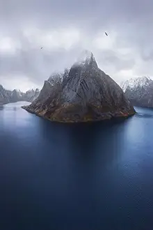 Inhabited Prints: Aerial view of calm water of sea washing island with rocky formations covered in snow under cloudy sky