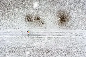 Aerial top down view at a colorful rainbow umbrella in the middle of a snow covered landscape at snowfall