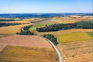 Aerial view of a country road amid fields against blue clear sky