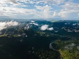River Hill Prints: Aerial view of curving river flowing through rural settlement located on coast with dense woods in hilly valley