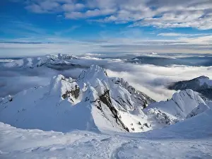 Aerial view of distant mountain peaks above clouds in clear sunny blue sky