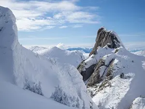 Aerial view of distant mountain peaks above clouds in clear sunny blue sky