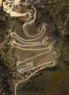 Serpentines Prints: Aerial view from a drone flying above a winding curved dirt road on mountainside