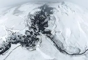 Uneven Prints: Aerial top view of fast streams flowing on uneven rocky terrain covered with snow on cold winter day in Iceland