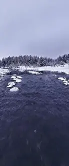 Forest River Prints: An aerial view of a frozen river flowing through snow-covered forests on a cloudy sunset sky background