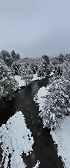 Forest River Prints: An aerial view of a frozen river flowing through snow-covered forests on a cloudy sunset sky background