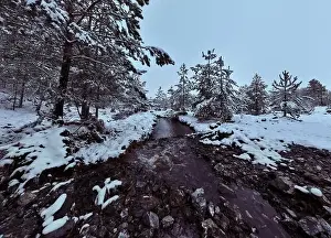An aerial view of a frozen river flowing through snow-covered forests on a cloudy sunset sky background