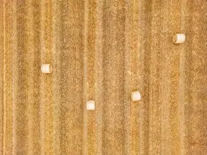 Pressing Prints: Aerial view of four hay bales on a dry stubble field with cracks in the ground