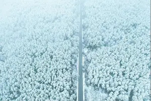 Aerial view of highway road through snow forest landscape in winter. Top view of highway motorway freeway from high attitude. Trip and travel concept