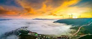 Morning Glow Prints: Aerial view top hill at dawn with fog covering small village in valley