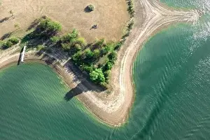 Aerial view of island with green trees and roads surrounded by sea or ocean with clear water