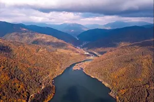 Aerial view on lake with turquoise water in Carpathian Mountains. Autumn forest with orange trees on coast