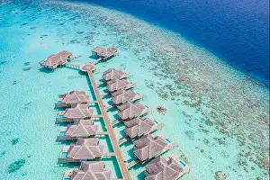 Aerial view of Maldives island, luxury water villas resort and wooden pier. Beautiful sky and ocean lagoon beach background. Summer vacation holiday