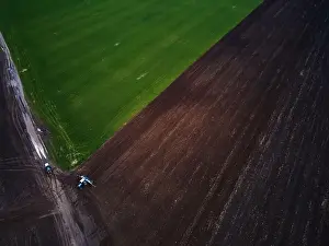 Sowing Prints: Aerial view of a modern green tractor plowing dry agricultural field