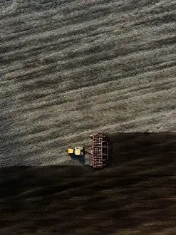 Sowing Prints: Aerial view of a modern yellow tractor plowing dry agricultural field