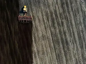Sowing Prints: Aerial view of a modern yellow tractor plowing dry agricultural field