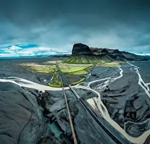 Aerial view of moody rugged volcanic Lomagnupur mountain and highway over glacier river