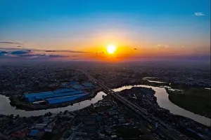 Warehouses Prints: Aerial view of the Ogun River snaking through the urban landscape under a vibrant sunset sky