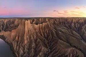 Aerial view of picturesque rough rocky mountains in daylight standing high next to canyon with flowing river under