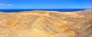 Deserts Prints: Aerial view of empty road crossing the desert mountains towards the blue Atlantic Ocean