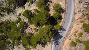 Aerial view of a rural countryside road stretching along bushes. Clip. Curving narrow road and stony ground