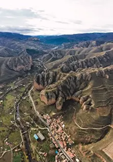 Aerial view of scenic green mountain slopes and buildings with road in valley