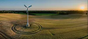 Wheat Field Prints: Aerial view of a small wind turbine gracefully spins above a gentle wheat field in atmosphere of a g