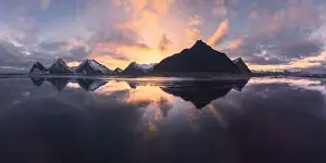 Aerial view of snow covered mountains located near sea with reflection in water against bright sky at sundown time in