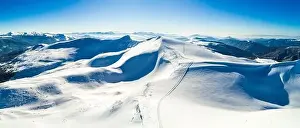 Mountain White Prints: Aerial view of a stunning snowy ski resort with snowy hills in the mountains and tourist site on a sunny clear morning