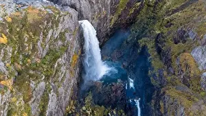 Aerial view of a stunning waterfall cascading down rocky cliffs into a deep blue pool surrounded by lush greenery