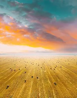 Aerial View Of Summer Hay Rolls Straw Field Landscape In Summer Sunny Day. Bright Orange Blue Sky Above Field Landscape. Harvest Season. Elevated View