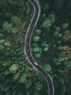 Aerial view taken by drone of a car driving on a forest road in autumn