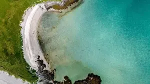 An aerial view of a white sand beach curving into a clear turquoise cove along the Norwegian coastline