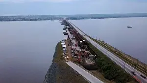 Aerial view of a wide river or lake crossed by the long narrow bridge with moving cars