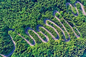 Aerial view of a winding mountain road passing through a fir trees forest