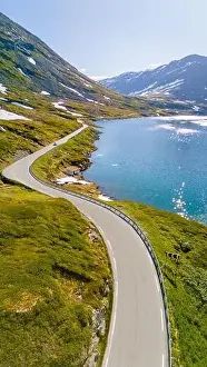 Scenic Drive Prints: An aerial view of a winding road snaking through green mountains and a glistening blue lake in Norway