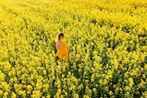 Aerial view of woman in yellow dress at blooming rapeseed field. Bright flowers and happy woman