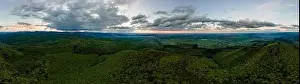 Aerial wide panoramic view of dark mountain hills covered with green mixed pine and lush forest in evening