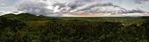 Aerial wide panoramic view of dark mountain hills covered with green mixed pine and lush forest in evening