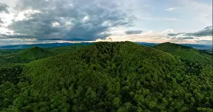 Aerial wide panoramic view of dark mountain hills covered with green mixed pine and lush forest in evening