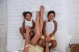 Siblings Prints: African American boy and girl are lying on white bed