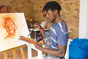 Easel Prints: African american male painter at work painting portrait on canvas in art studio