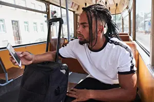Baggage Prints: An African American man using a smartphone sits on a tram at Viena Railway