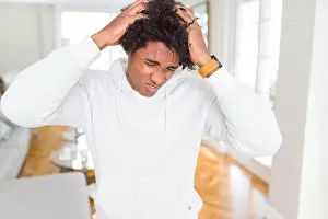 Suffering Prints: African American man wearing sweatshirt suffering from headache desperate and stressed because pain and migraine