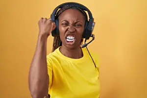 Braids Prints: African american woman listening to music using headphones angry and mad raising fist frustrated
