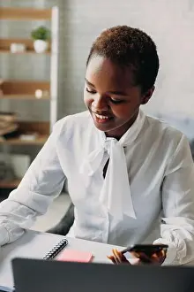 Accountant Prints: African businesswoman with laptop writing something in notebook while using the mobile phone