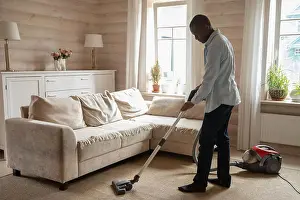Abode Prints: African guy use vacuum cleaner cleaning carpet in living room