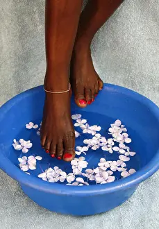 Posed Prints: African woman soaking her feet in bowl of water and flower pedals