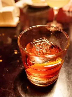 Old Black Prints: alcoholic cocktail with ice cube in glass glass on bar table illuminated by electric light close up