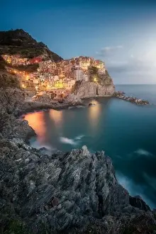 Amazing landscape with small town with colorful lights on rocky coast washing by tranquil ocean water at night